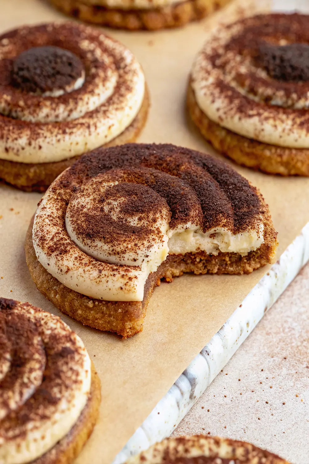 Gluten-free tiramisu cookies with swirled mascarpone cream topping and cocoa powder dusting on a white serving platter